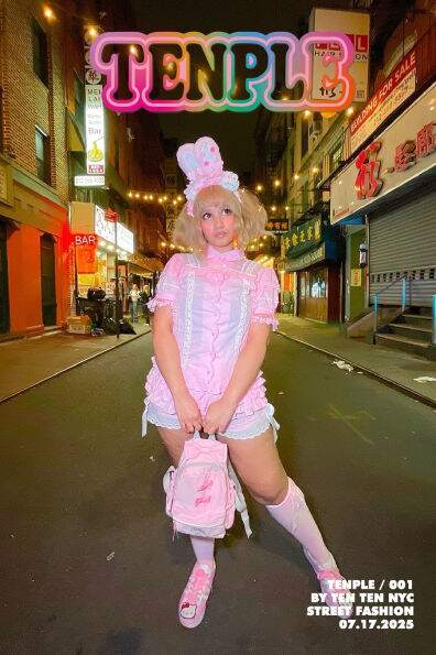 A feminine model in pink frilly clothing standing in the center of a street. The cover of TENPLE.